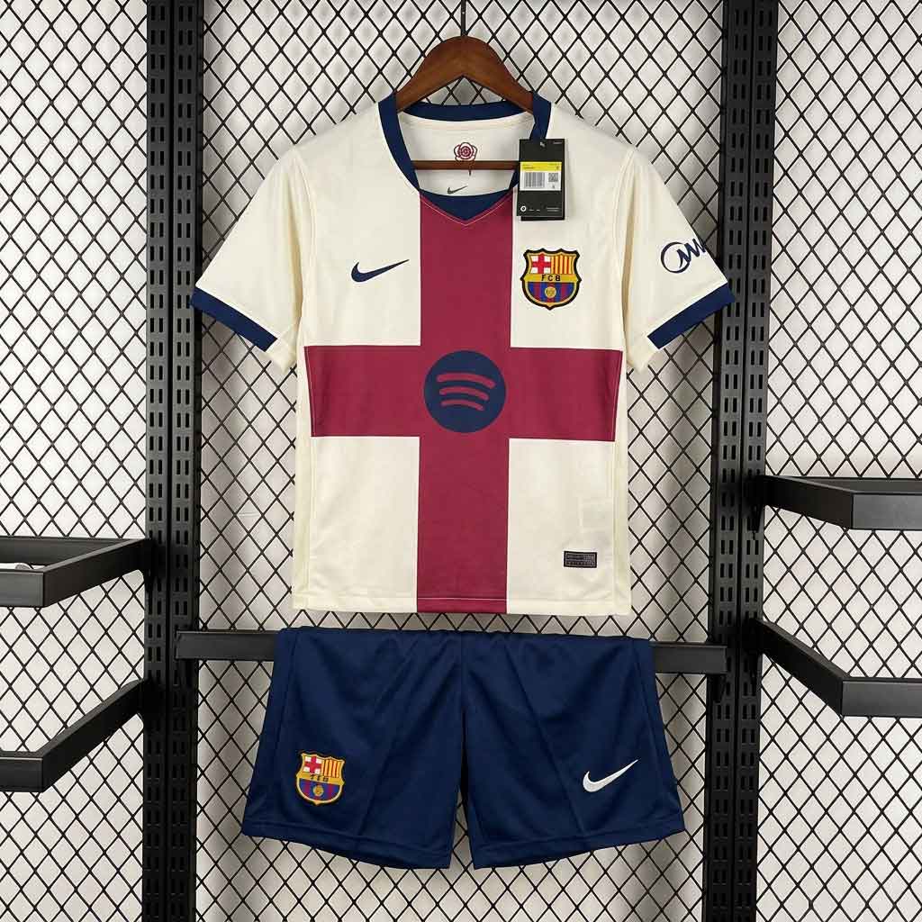 Detský futbalový set FC Barcelona pre sezónu 2026/27 pozostávajúci z krémového dresu s červeným krížom Sant Jordi a tmavomodrých šortiek.